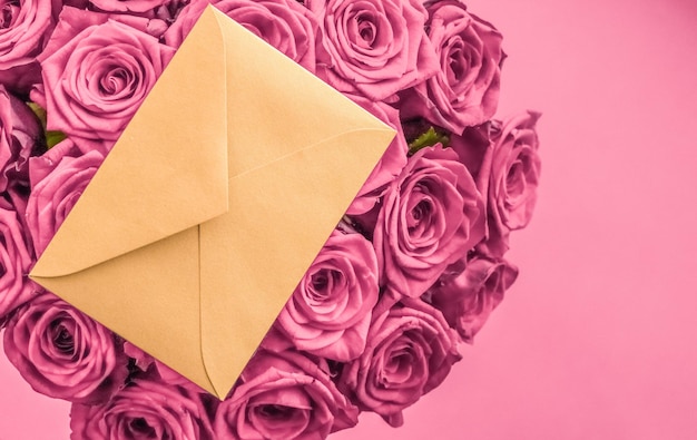 Lettera d'amore per le vacanze e consegna di fiori bouquet di lusso di rose e carta su sfondo rosa cipria per un design romantico per le vacanze