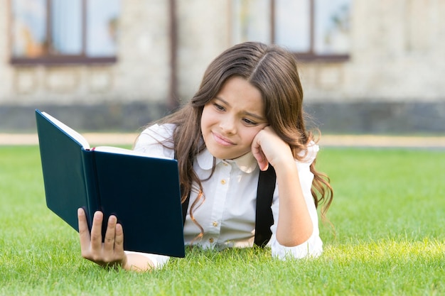 Letteratura per bambini Lezione all'aria aperta Libro di lettura per bambini piccoli e carini all'aperto Uniforme scolastica per scolaretta sdraiata sul prato con il libro preferito Concetto di studio Istruzione di base Libro educativo