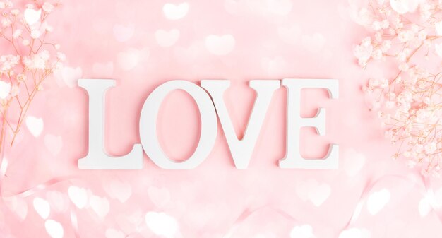Lettere bianche LOVE con cornice di gipsofila bianca delicata su rosa pastello con cuori di luci bokeh