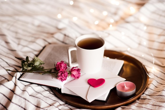 Lettere d'amore con rose e tazza di caffè sul libro aperto a letto. San Valentino. Buon giorno.