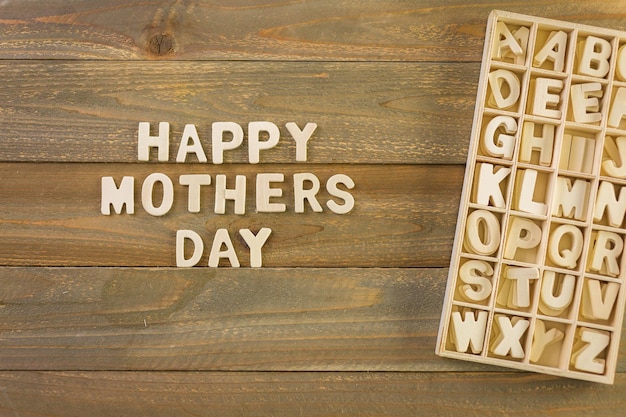 Lettere di legno incompiute firmano Happy Mother's Day su uno sfondo di legno dipinto.