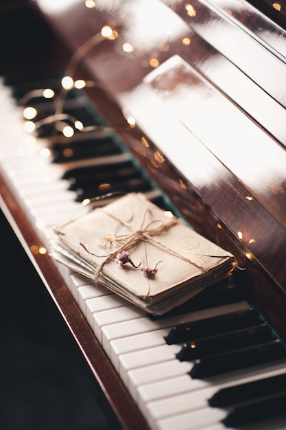 Lettere di posta lumache di carta in busta sui tasti del pianoforte con fiori secchi sopra bagliore Luci di Natale primo piano Stile di vita romantico San Valentino