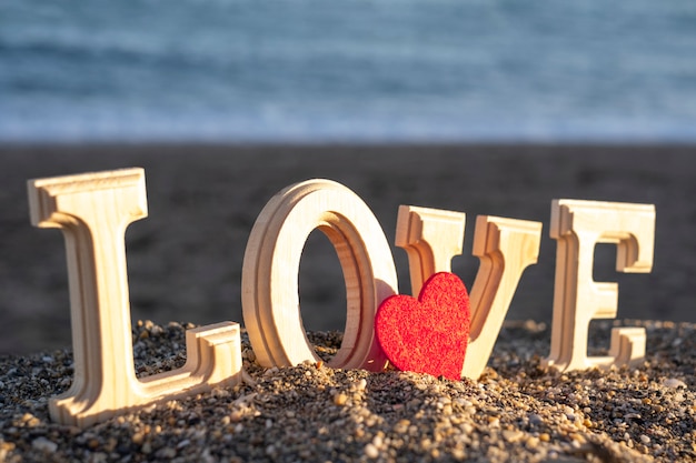 Lettere in legno che formano la parola amore con un cuore rosso in riva al mare. concetto di amanti