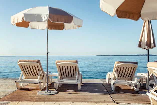 Lettini con ombrelloni sul molo sullo sfondo del mare. Relax e piacere.