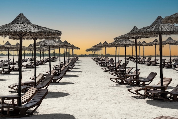 Lettini e ombrelloni in spiaggia Lettini da spiaggia tropicale e ombrelloni con palme concetto di vacanza al tramonto