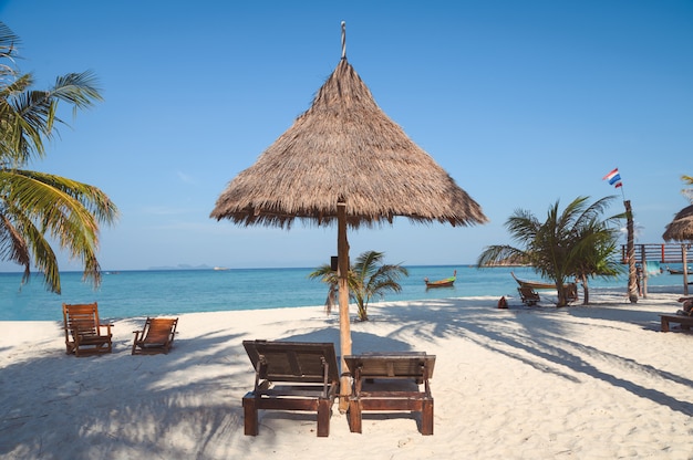 Lettino in ombrellone di paglia sulla spiaggia tropicale