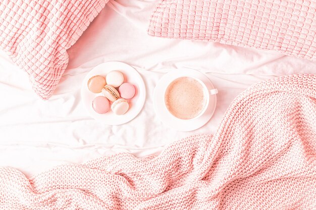 Letto con plaid a maglia rosa, caffè e amaretti, vista dall'alto, copia spazio, piatto.