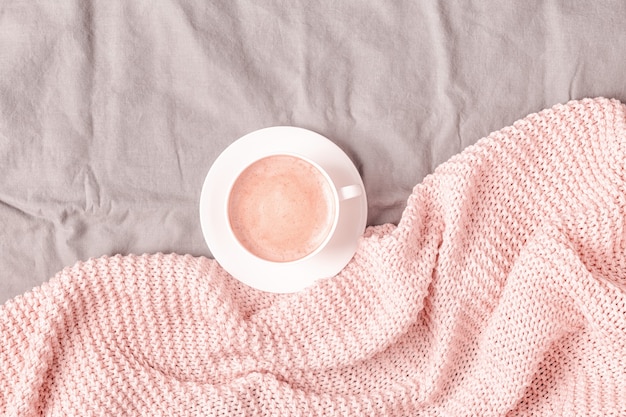 Letto con plaid lavorato a maglia rosa e caffè