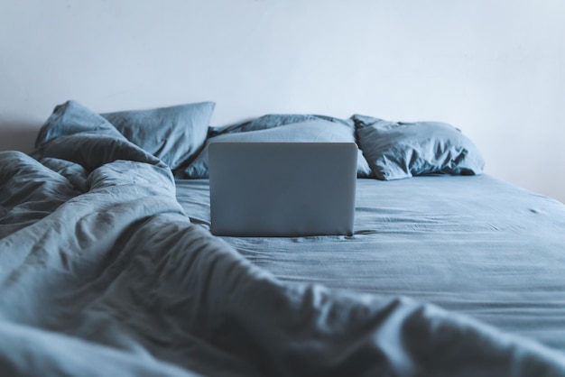 Letto grigio disordinato vuoto con il computer portatile. stile di vita resto a letto concetto