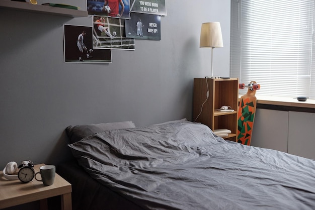 Letto matrimoniale con cuscini grigi e lenzuola in piedi vicino al muro con poster di giocatori di calcio in camera da letto