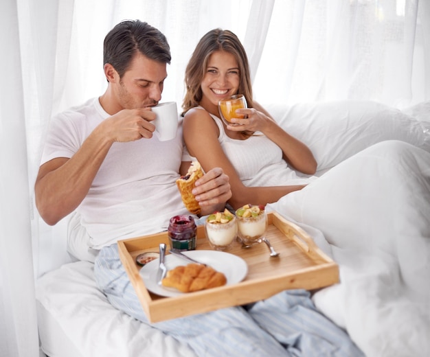 Letto per la colazione e ritratto di coppia con cura dell'amore e cibo mattutino insieme a casa La felicità sorride e rilassa i giovani che mangiano e bevono in una casa per l'anniversario o il giorno di San Valentino