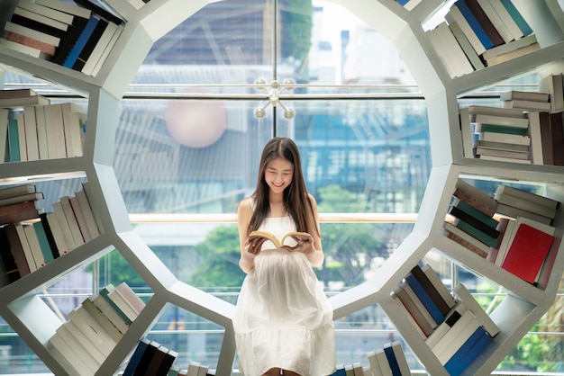 Lettura asiatica della ragazza su uno scaffale per libri in una biblioteca nella sua università