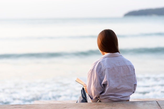 Lettura della donna di vista posteriore sulla spiaggia