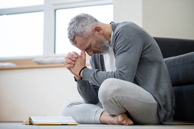 Letture spirituali. Un uomo dai capelli grigi seduto sul pavimento e dall'aspetto pensieroso