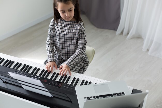 Lezione a casa sulla musica per la ragazza al pianoforte. L'idea delle attività per il bambino a casa durante la quarantena. Concetto di musica