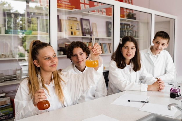 Lezione di chimica Studentessa e compagni di classe tengono la boccetta per esperimenti e sorrisi in laboratorio Istruzione scolastica