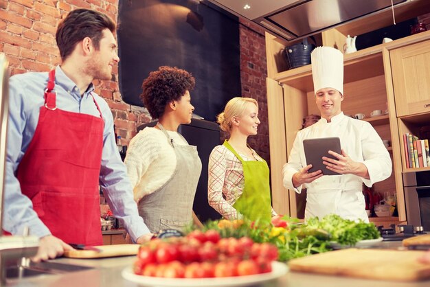 lezione di cucina, cucina, cibo, tecnologia e concetto di persone - amici felici con tablet pc in cucina