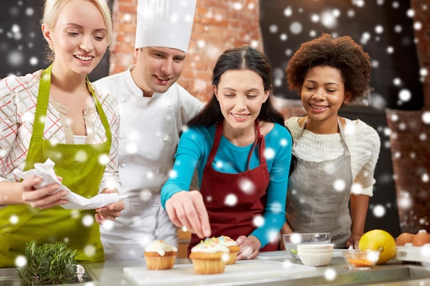 lezione di cucina, cucina, prodotti da forno, cibo e concetto di persone - felice gruppo di donne e chef maschi che cucinano in cucina sopra l'effetto neve
