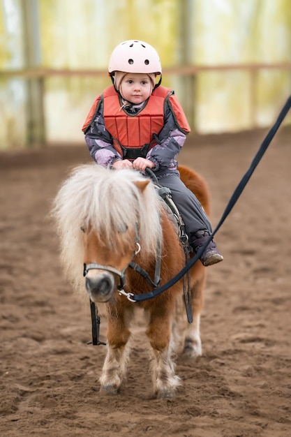 Lezione di equitazione per bambini Una bambina di tre anni cavalca un pony e fa esercizi