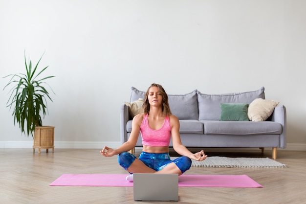 Lezione di yoga online. Donna nella posizione del loto davanti al monitor del laptop.