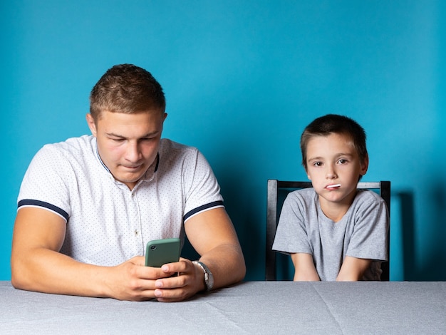 Lezioni a casa con il bambino papà è distratto dal telefono mentre il figlio si annoia