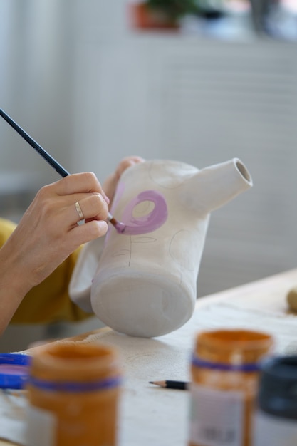 Lezioni d'arte intrattenimento donna artigiana che decora la brocca di vasaio con vernice e pennello in officina