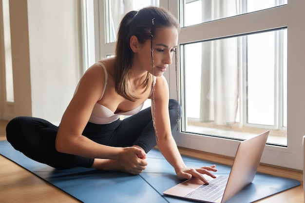 Lezioni di yoga online Ragazza di yoga positiva che fa pratica mattutina davanti al laptop a casa