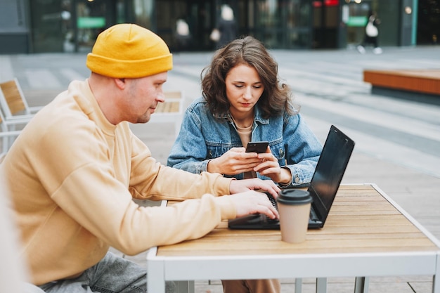 Liberi professionisti alla moda di giovani coppie che lavorano al computer portatile nel caffè della via