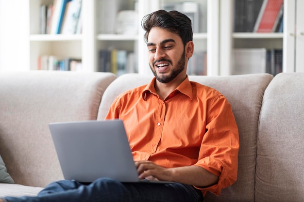 Libero professionista arabo felice che lavora da casa usando il computer portatile