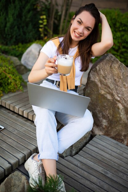 Libero professionista attraente giovane donna in pausa pranzo seduto con il computer portatile in giardino.