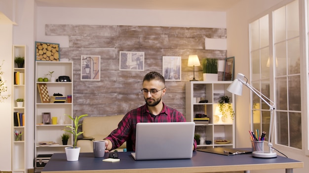 Libero professionista caucasico bello che lavora al computer portatile dall'ufficio domestico.