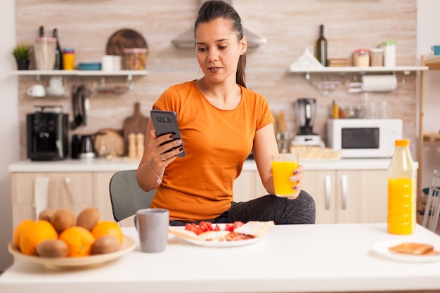 Libero professionista che beve succo d'arancia fresco al mattino mentre controlla la posta elettronica sullo smartphone