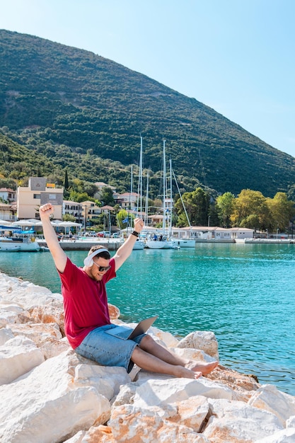 Libero professionista dell'uomo che lavora al computer portatile all'estate della panchina del porto della città