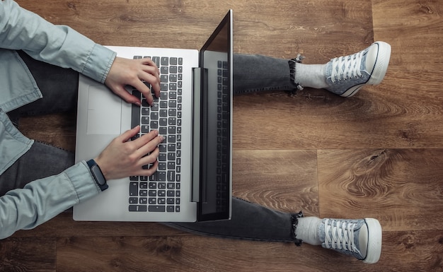 Libero professionista della donna che si siede su un pavimento di legno e che digita sul computer portatile.