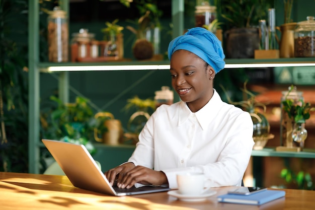 Libero professionista della donna di colore che digita sul computer portatile mentre si siede al caffè