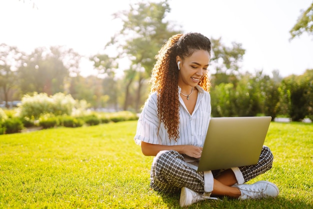 Libero professionista della giovane donna che si siede sull'erba verde con il computer portatile Istruzione online