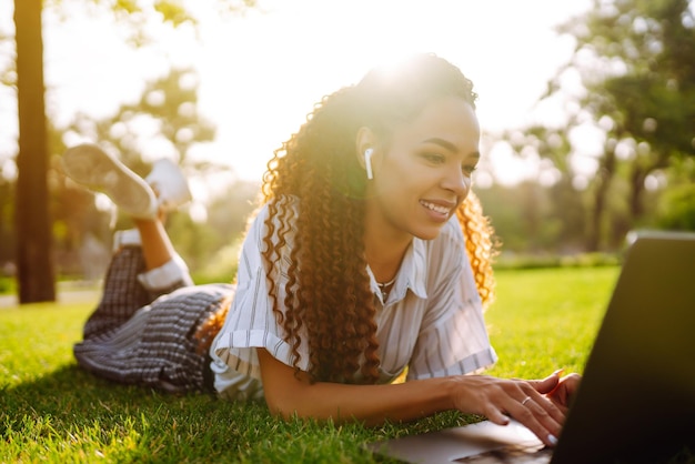 Libero professionista della giovane donna che si siede sull'erba verde con il computer portatile Istruzione online