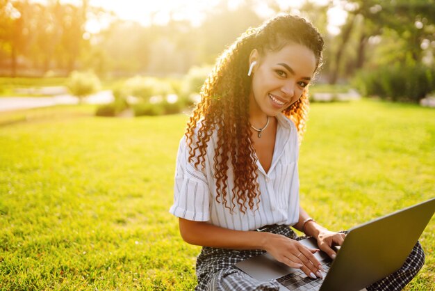 Libero professionista della giovane donna che si siede sull'erba verde con il computer portatile Istruzione online