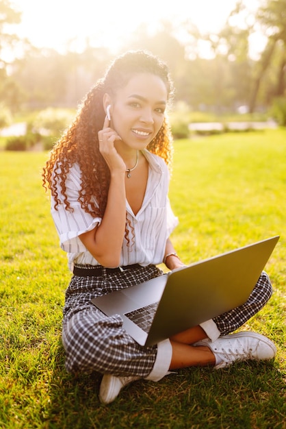 Libero professionista della giovane donna che si siede sull'erba verde con il computer portatile Istruzione online