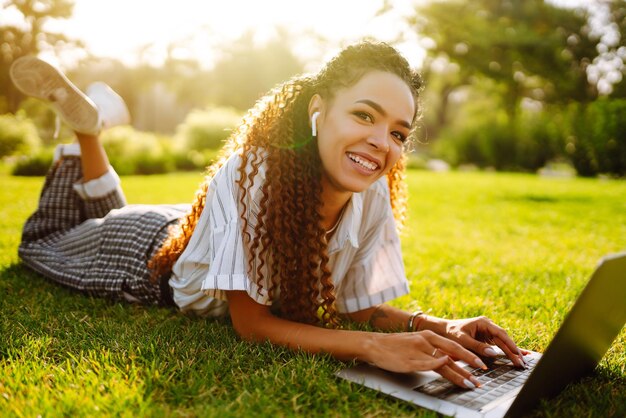 Libero professionista della giovane donna che si siede sull'erba verde con il computer portatile Istruzione online
