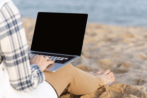 Libero professionista donna irriconoscibile che lavora su herlaptop sulla spiaggia