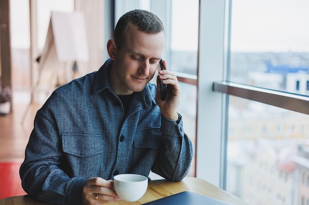 Libero professionista europeo nel controllo della notifica sullo smartphone sulle transazioni di denaro che fanno affari online lavorando in remoto mentre si trova al bar e beve caffè