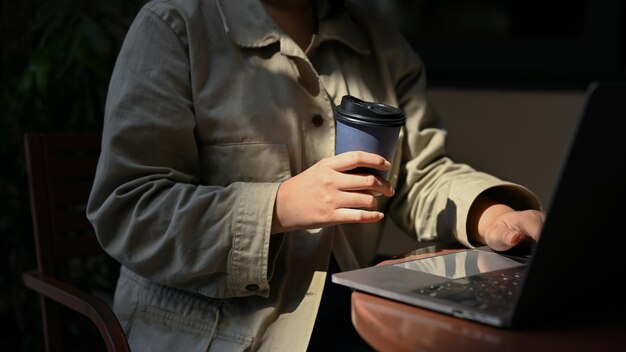 Libero professionista femminile che lavora a distanza presso la caffetteria sorseggiando caffè mentre si utilizza il suo laptop