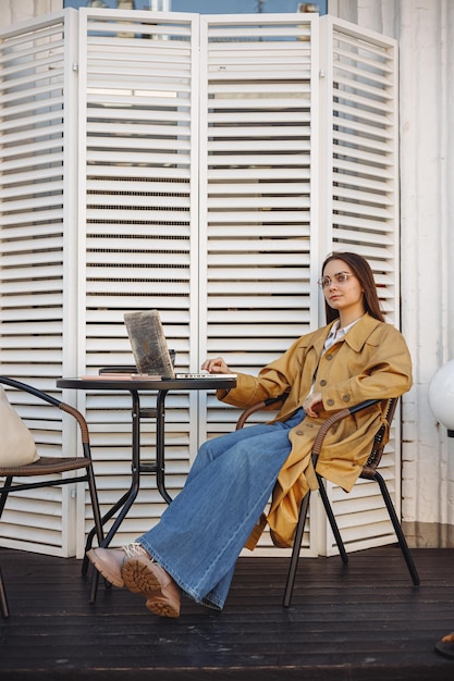 libero professionista femminile seduto al tavolo con il computer portatile sulla terrazza del caffè all'aperto