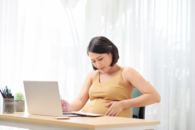 Libero professionista incinta che tocca la pancia vicino al computer portatile