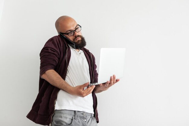 Libero professionista maschio occupato che parla al telefono e che tiene un computer portatile Ritratto di un bell'uomo calvo barbuto