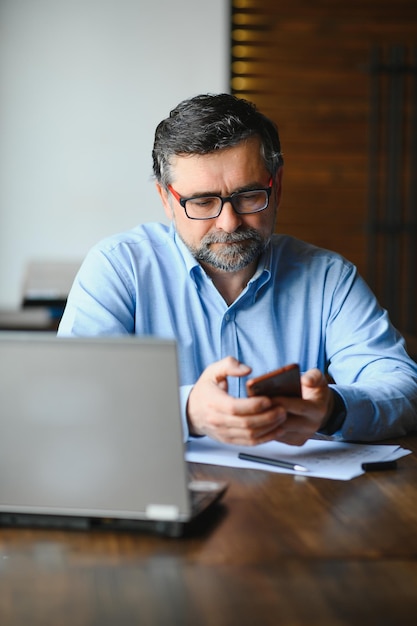 Libero professionista maschio sta lavorando in un bar su un nuovo progetto di affari Si siede a una grande finestra al tavolo Guarda lo schermo di un laptop con una tazza di caffè