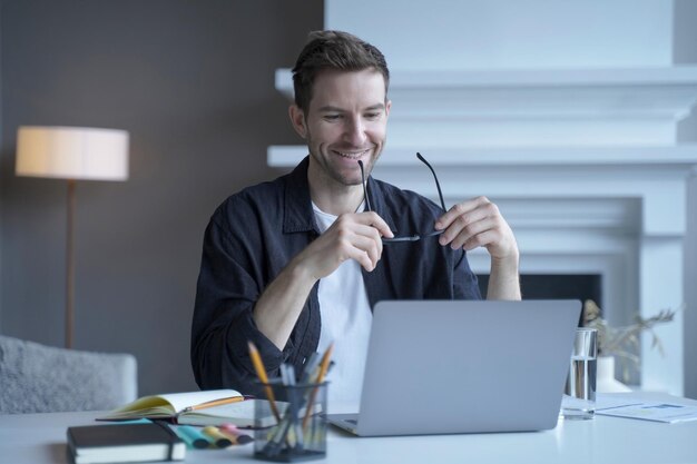 Libero professionista tedesco uscito che guarda sul laptop con un sorriso felice mentre tiene gli occhiali in mano