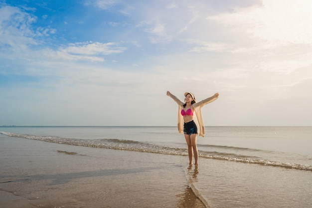 Libertà donna in bikini che cammina con le braccia alzate sulla spiaggia del mare