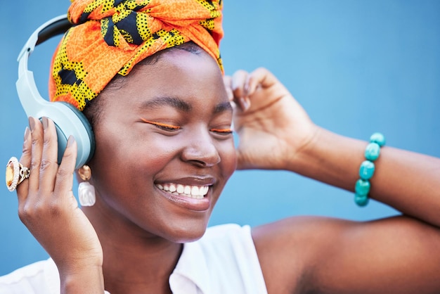 Libertà musicale e cuffie con una donna di colore all'aperto su uno sfondo di parete blu che si gode una traccia Radio rilassati e felice con una giovane donna che trasmette in streaming o ascolta l'audio su un auricolare wireless